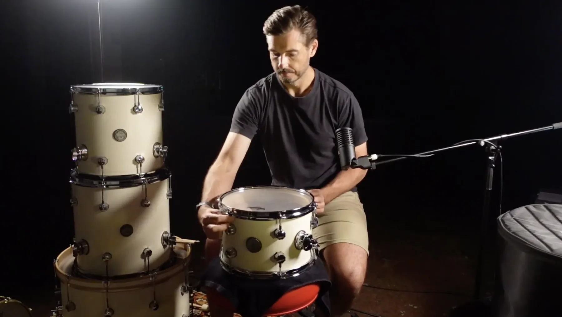 Stan Bicknell teaching his drum tuning course, adjusting the tension on a tom beside a stack of drums